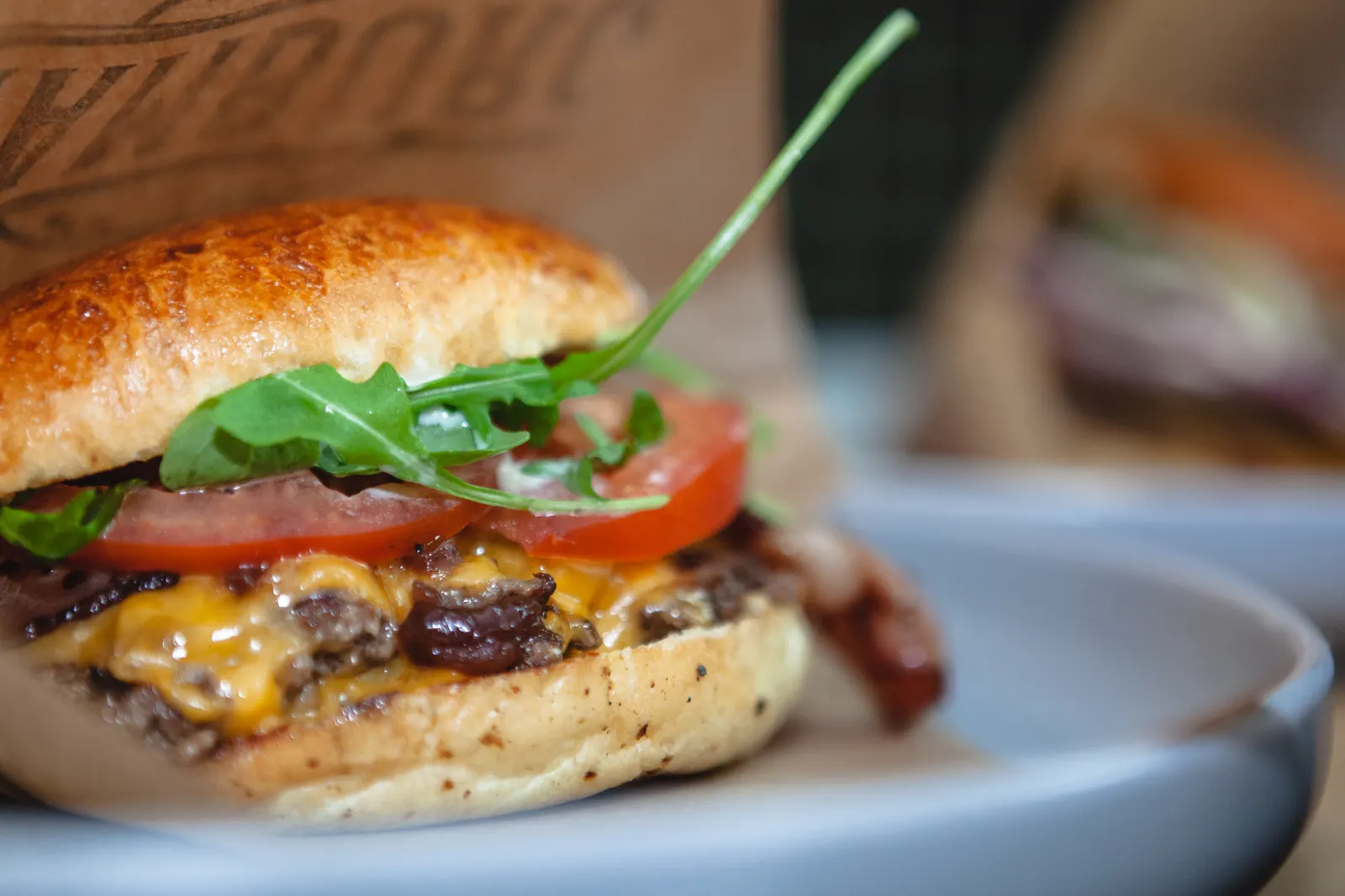 Foto de ejemplo: smash burger doble con cheddar fundido, tomate y rúcula, de cerca sobre un plato