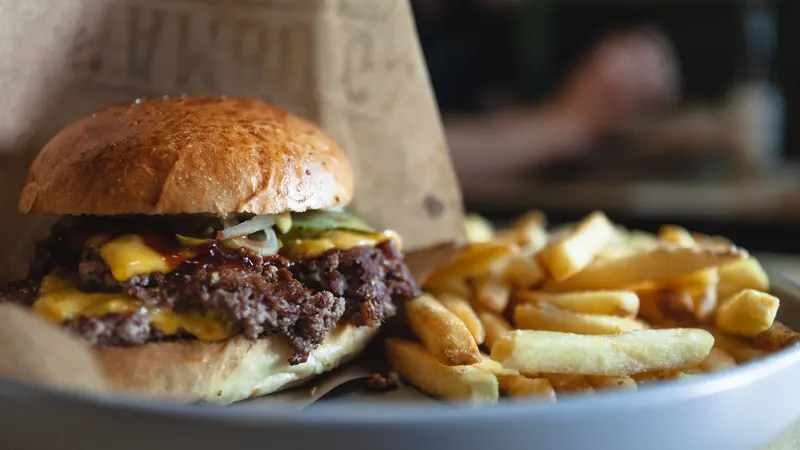 Foto de ejemplo: smash burger doble con cheddar y pepinillo junto a un montón de patatas fritas