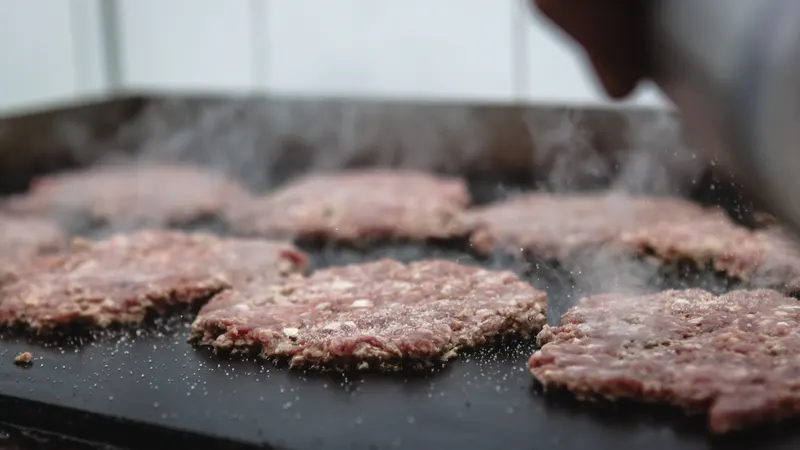 Foto de ejemplo: varias hamburguesas chafadas se tuestan en la plancha con vapor